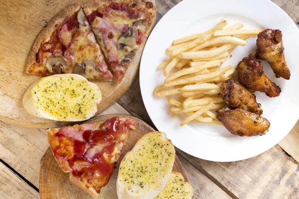 Fast food, ali di pollo croccanti, pane, patatine fritte e pizza su — Foto Stock