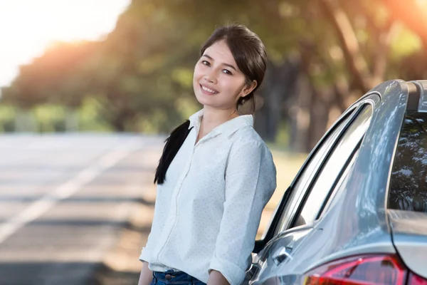 アジアの若い女性に立って、彼女の車の側で休んで — ストック写真