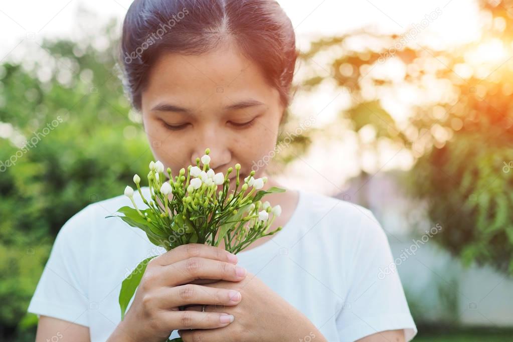 Asian woman smelling flowers in garden.