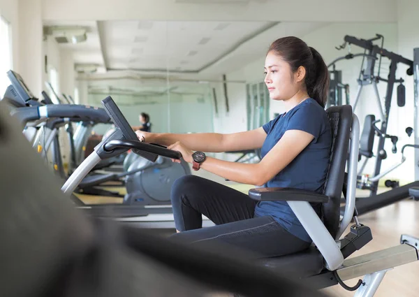 Mujer asiática montando bicicleta estacionaria en el gimnasio . —  Fotos de Stock