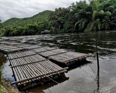Akan nehirde park etmiş bambu botu. Arka planda bambu ve dağlar var..