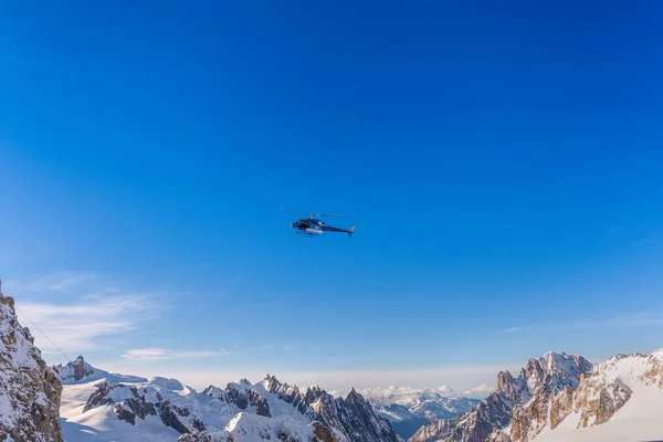 青い空に対して晴れた日に雪に覆われた山頂上の飛行中の青いヘリコプター — ストック写真