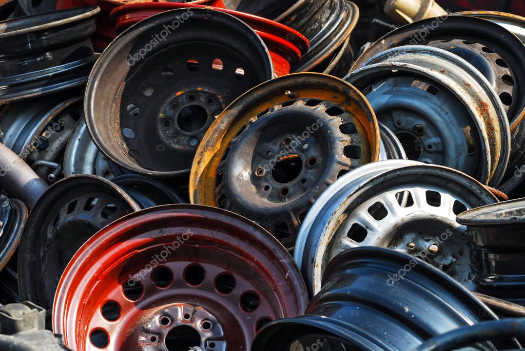 Old hubcaps with no logo. Some rusty, some not. In a heap and abandoned. Red one in front. No visible logo or brand.