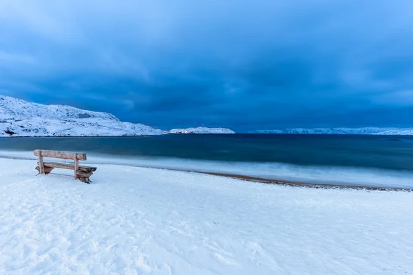 黄昏时分 在覆盖着积雪的海滩上俯瞰大海的孤零零的木制长椅 — 图库照片