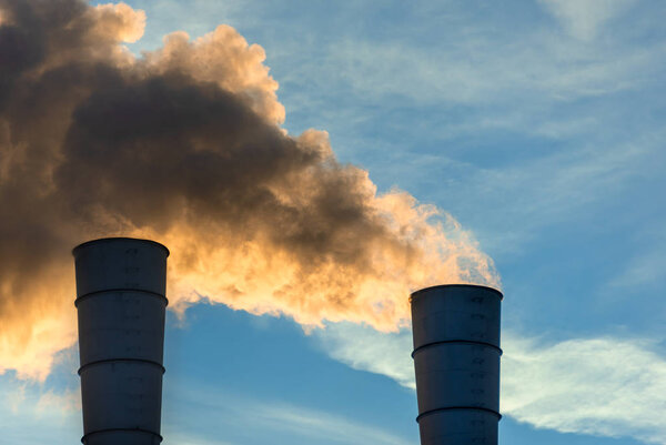 Industrial chimneys spewing smoke and soot in the blue sky polluting the air and causing global warming and climate change with greenhouse gasses and CO2 emissions