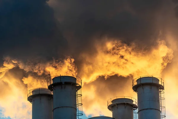 青空の中で煙やすすを噴き出す工業用煙突は大気を汚染し 温室効果ガスやCo2排出量で地球温暖化や気候変動を引き起こします — ストック写真