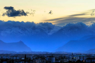 View of Turin (Torino) Italy at sunset looking toward Susa Valley with the backdrop of the Italian Alps and the Sacra di San Michele Church silhouetted clipart