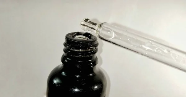 A close up photo of a medical dropper bottle isolated on white background, the dropper is dropping the liquid into the black bottle