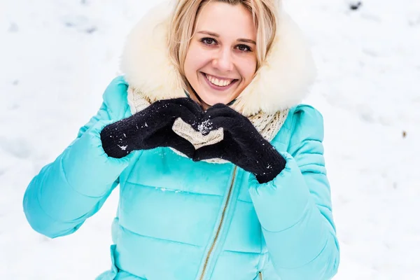 Το χειμώνα. Ξανθιά κοπέλα κοντά στο χιόνι δείχνει καρδιά — Φωτογραφία Αρχείου