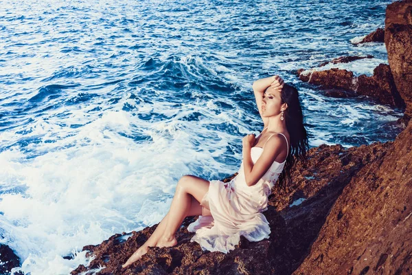 Girl with bare feet sitting on the rocks by the sea — Stock Photo, Image