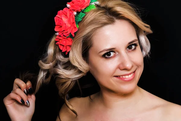 Mujer con rubia tendida y adornada con flores rojas sobre un fondo oscuro — Foto de Stock