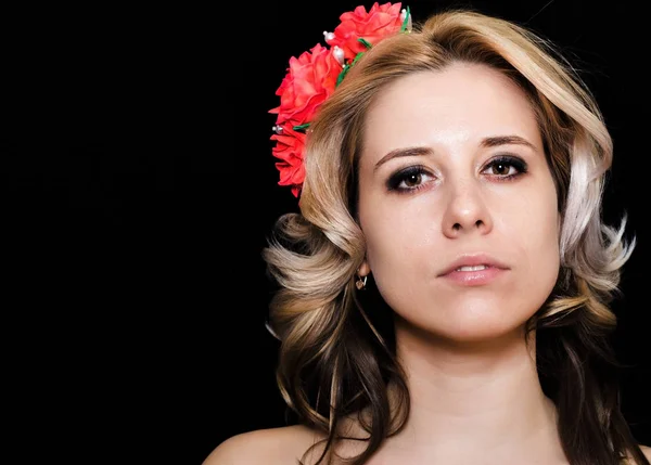 Mujer con rubia tendida y adornada con flores rojas sobre un fondo oscuro — Foto de Stock