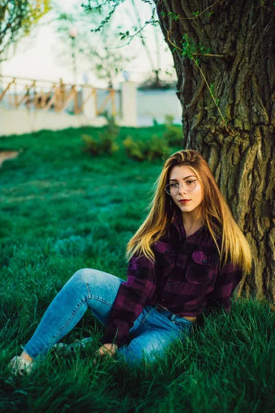 Blondes Mädchen im Park sitzt unter einem Baum — Stockfoto