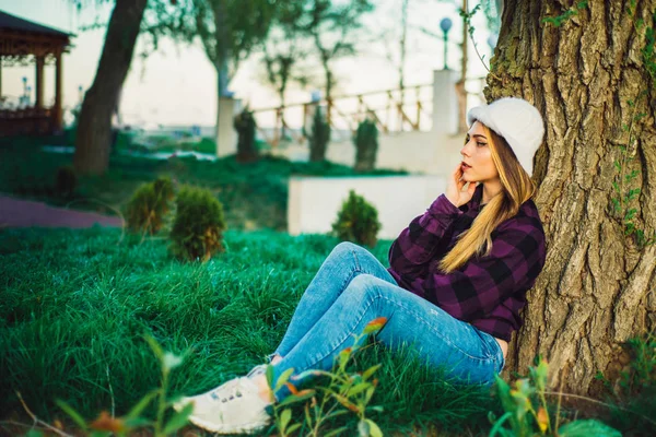 Blondes Mädchen im Park sitzt unter einem Baum — Stockfoto