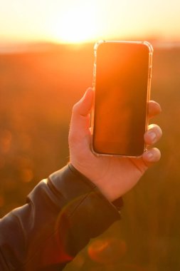 Telefonu güneşin arka planında tutan el. Yakın plan.