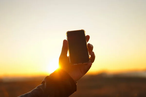 Hand holds the phone on a background of the sun. Close-up