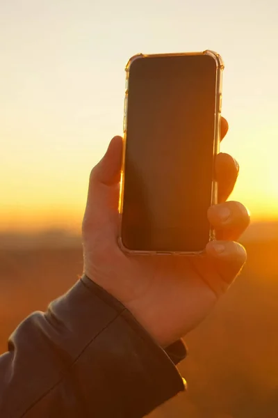 Hand holds the phone on a background of the sun. Close-up
