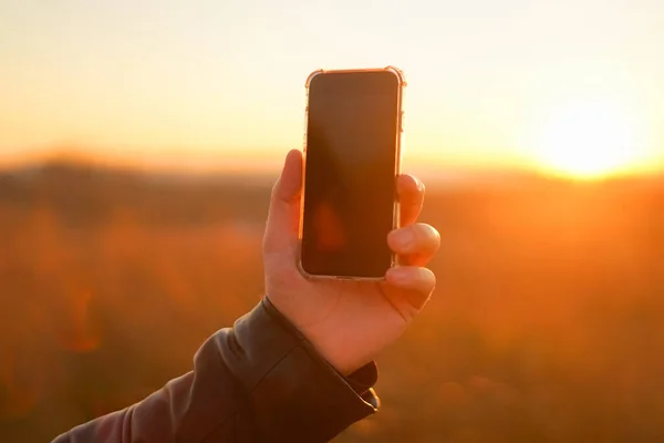 Hand holds the phone on a background of the sun. Close-up