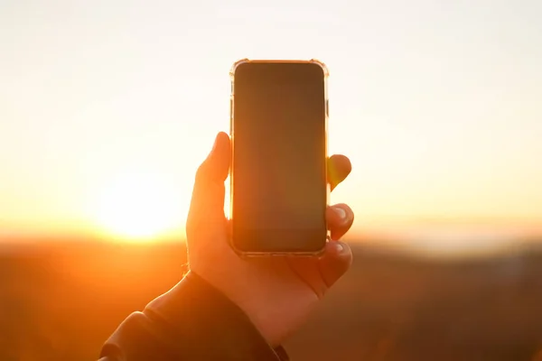 Hand holds the phone on a background of the sun. Close-up