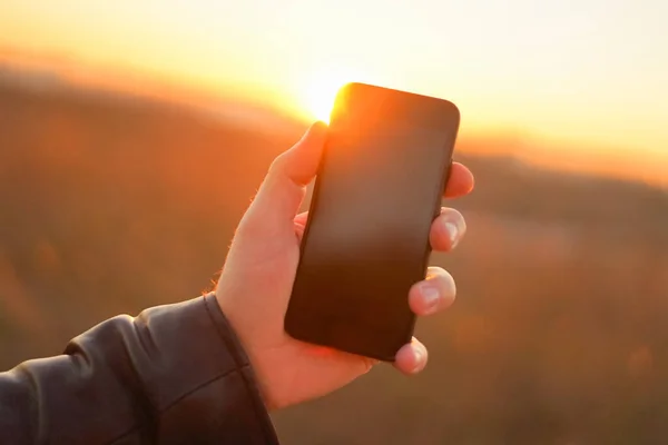 Hand holds the phone on a background of the sun. Close-up