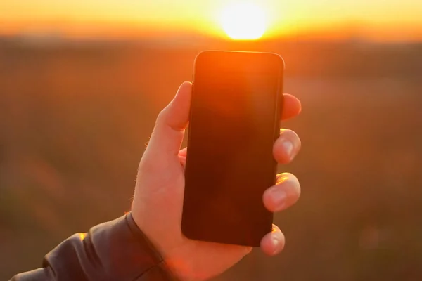 Hand holds the phone on a background of the sun. Close-up