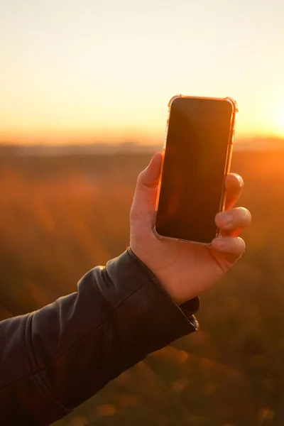 Die Hand Hält Das Telefon Auf Dem Hintergrund Der Sonne Stockbild