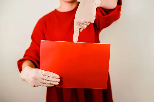 Woman on a red background in medical gloves holds a red poster. Close-up