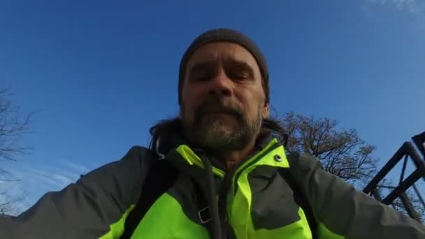 Volwassen mannelijke wielrenner met baard rijdt fiets tegen de blauwe lucht en bomen stad — Stockvideo