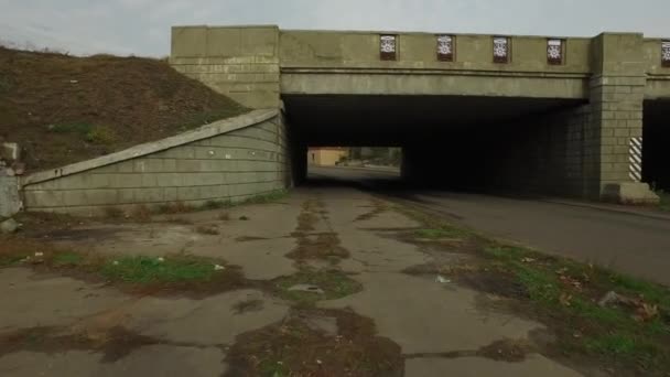 Verkeer van een fietser met een camera onder een concrete spoorwegbrug — Stockvideo