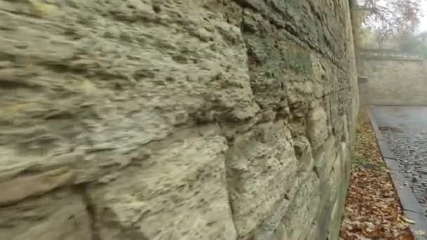 壁の間の花崗岩舗装に沿ってシェルレンガの石の古い壁に沿って移動します 光霧の秋の街 — ストック動画