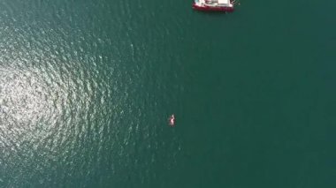 Deniz / okyanusun su yüzeyinin havadan görünüşü. Çok aşağıda bir motorlu tekne ve kırmızı katamaran gemisi.