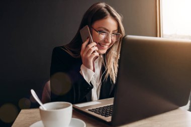Ofis kıyafetleri içinde harika bir gülümsemeyle telefonda konuşan, kafede yalnız başına güzel bir kız.