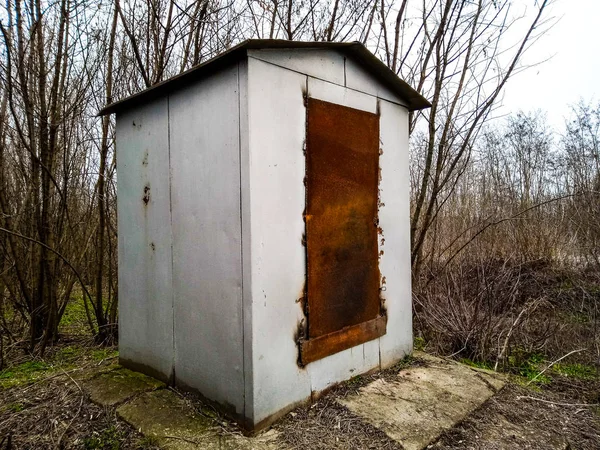 A metal booth with rusty doors stands in a forest belt
