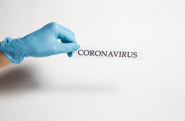 Tıbbi eldivendeki bir el beyaz arka planda Coronavirus yazısını tutar.