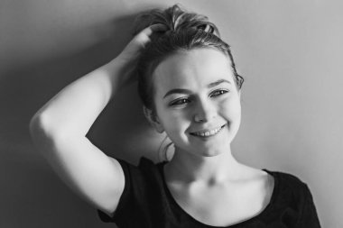 Genç, gülümseyen bir kız elini mavi duvara dayar. Siyah beyaz fotoğraf..