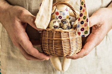 Mutlu Paskalyalar, keten arka planda sepetteki bıldırcın yumurtaları ve erkek ellerinde tavşan, bahar Ortodoks ve Katolik bayramı.