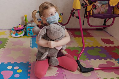 Üzgün bir çocuk ve koruyucu tıbbi maskeli pelüş fili oyun evinde yürümeden oturuyorlar. Koronavirüs enfeksiyonunu önlemek için karantinada kalın. Covid Salgını