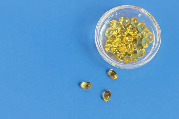 Yellow gelatin capsules with vitamin D3 in a glass container on a blue background. Pharmaceutical therapeutic and prophylactic preparation of vitamin D deficiency in adults and children