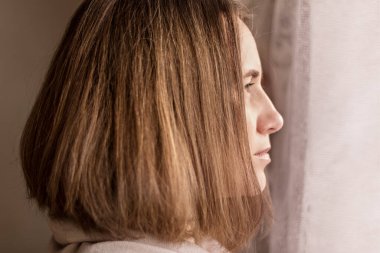 Üzgün bir kız, kendini izole ettiği için evinin penceresinden dışarı bakar. Koronavirüs enfeksiyonunu önlemek için karantinada kalın. Covid-19 Salgını 2020