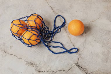 Portakallar gri arka planda, eko-ağlı mavi bir çantada. Çevre bakımı, atık geri dönüşümü