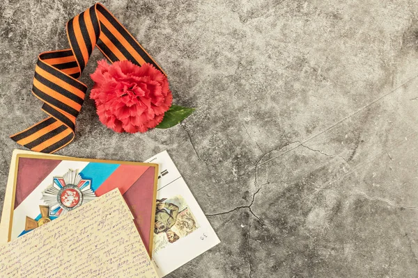Kırmızı karanfil, 9 Mayıs 'ın sembolü Aziz George kurdelesi, eski kartpostal ve heykelin gri mermerinin üzerinde ön tarafından gelen mektuplar. Zafer Günü. 75 yıl..