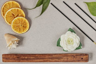 Tütsü standı olan çubuklar, gri arka planda tahta bir kasede dilimlenmiş turuncu halkalar. Ayrıca çiçek ve deniz kabuğu şeklinde bir mum. Romaterapi. Ev Kaplıcası konsepti.