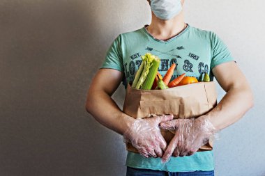 Bir adam elinde alışveriş poşeti olan bir eco kağıdı tutuyor. Eve kurye ile yemek teslimatı. Eldivenli eller. Coronavirus, COVID 19