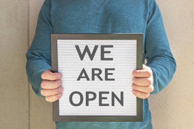 Bir adam içinde hoş geldin mesajı olan bir pankart tutuyor. Biz açığız. Karantinanın sonu. Otel, kafe, yerel mağaza, hizmet sahibi, Coronavirus salgınından ve izolasyondan sonra misafirlerle tanışıyor.