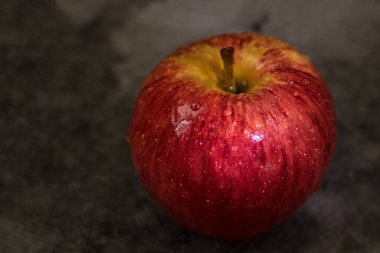 Koyu arkaplan üzerinde su damlacıkları olan sulu, taze kırmızı elma.