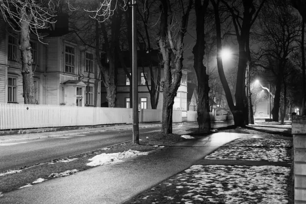 The street leading to the park is lit by the lamp lights at Tallinn, the capital of Estonia. The lights create dramatic shadows on the walls of the old wooden houses.