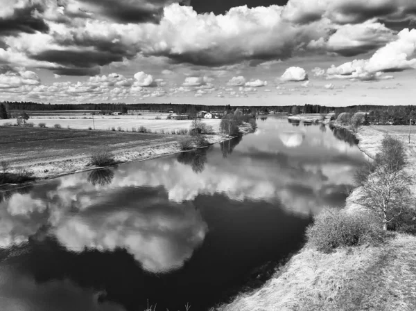 The beautiful clouds reflect on the still water of the river at the rural Finland. The spring weather is slowly getting warmer.