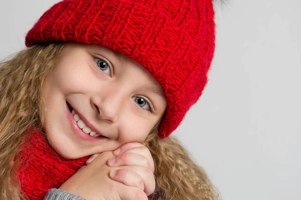 Retrato de una hermosa niña en sombrero de punto rojo sobre un fondo gris. Rostro de un niño feliz de cerca — Foto de Stock