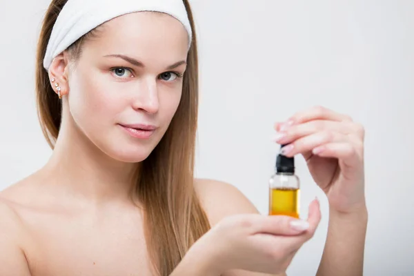 Portrait of a beautiful young woman with facial oil in hands