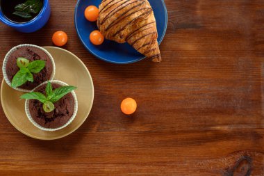 Sabah kahvaltısı: mavi bardak çay, çikolata kruvasan, kekler ve physalis ahşap bir masa üzerinde. Düz kompozisyon